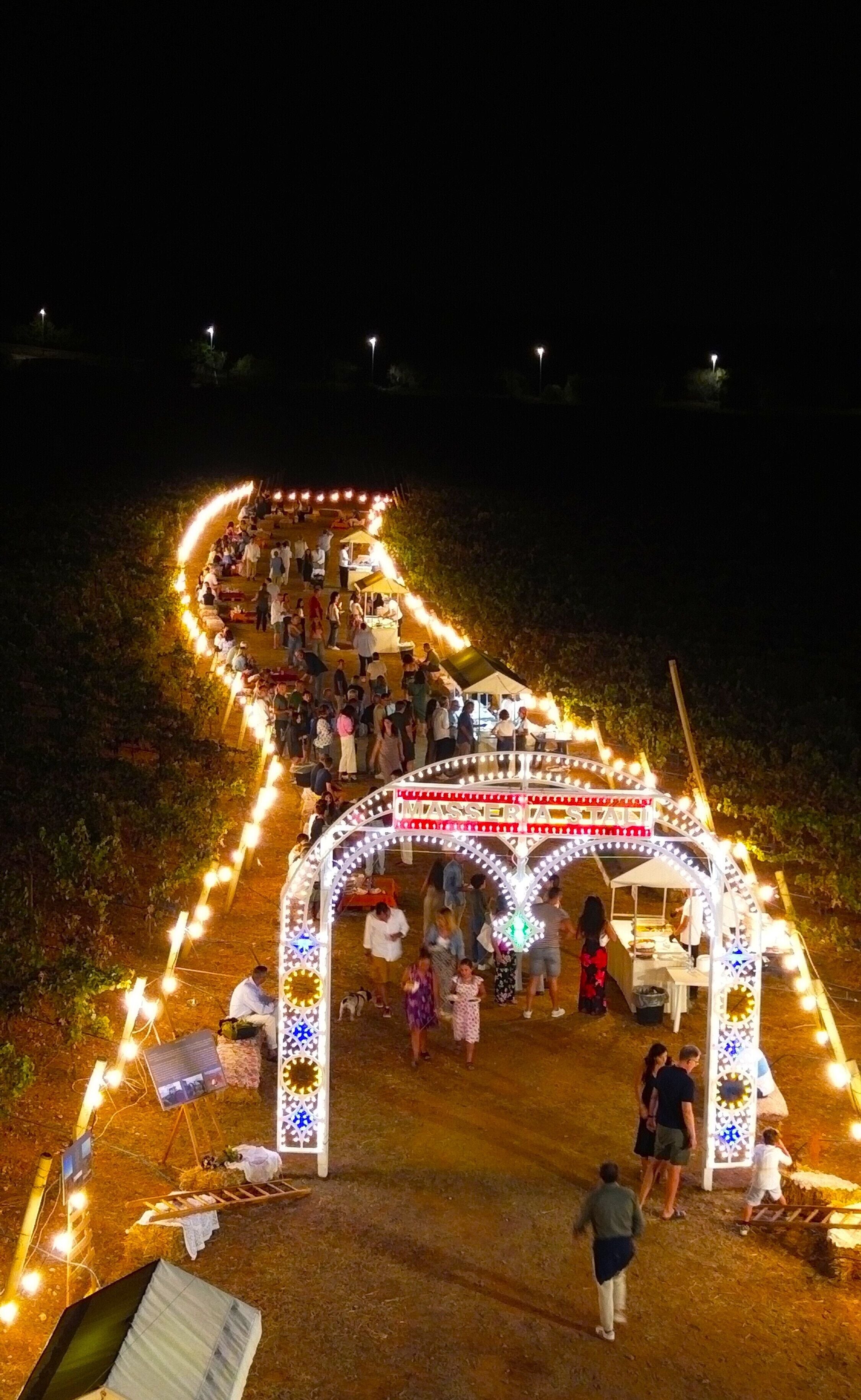A nighttime outdoor event with a decorated archway and people gathered around.