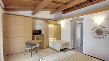 Une petite pièce comprenant un lit, un bureau et une chaise. Un téléviseur est fixé au mur, ainsi qu’un élément décoratif.