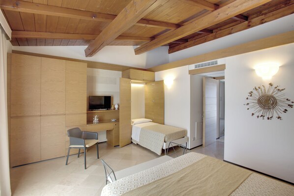 A compact room with a bed, a desk, and a chair. There is a television on the wall and a decorative wall piece. - Masseria Stali, The Originals Relais (Caprarica di Lecce)