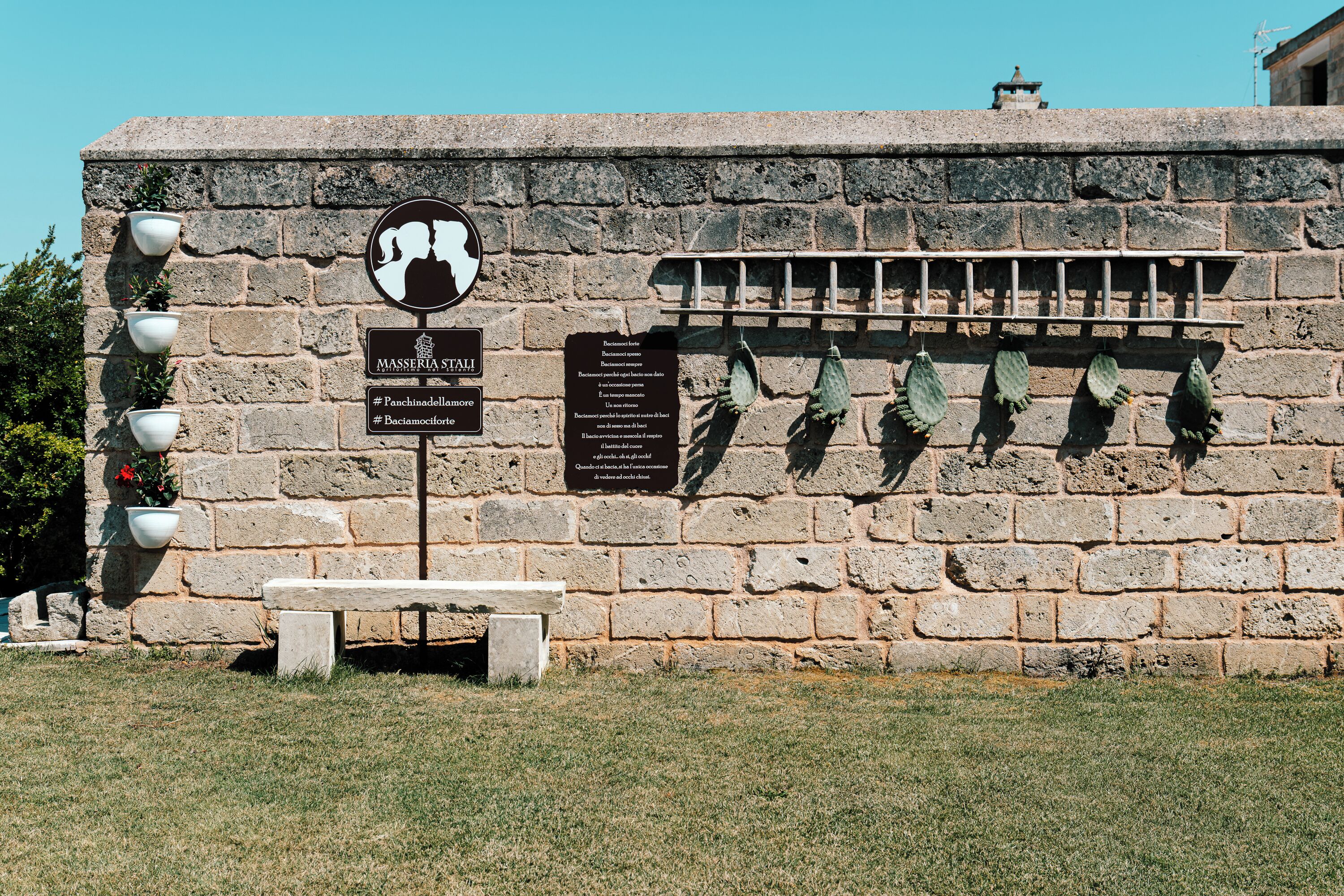 A stone wall with a bench, potted plants, and informational signs.