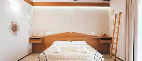 A bedroom with a wooden headboard, a bed with neatly folded towels, a bedside table with a lamp, and a ladder against the wall.