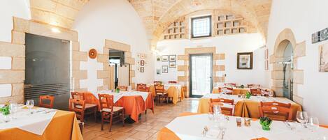 A restaurant with stone arches, tables with orange tablecloths, and a high ceiling.