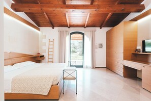 Une chambre avec un plafond en bois, un lit recouvert d’une couvre-lit à motifs, un bureau avec une télévision et une vue par la fenêtre.