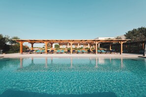 Une piscine d’un bleu éclatant, avec des chaises longues disposées sous une pergola en bois.