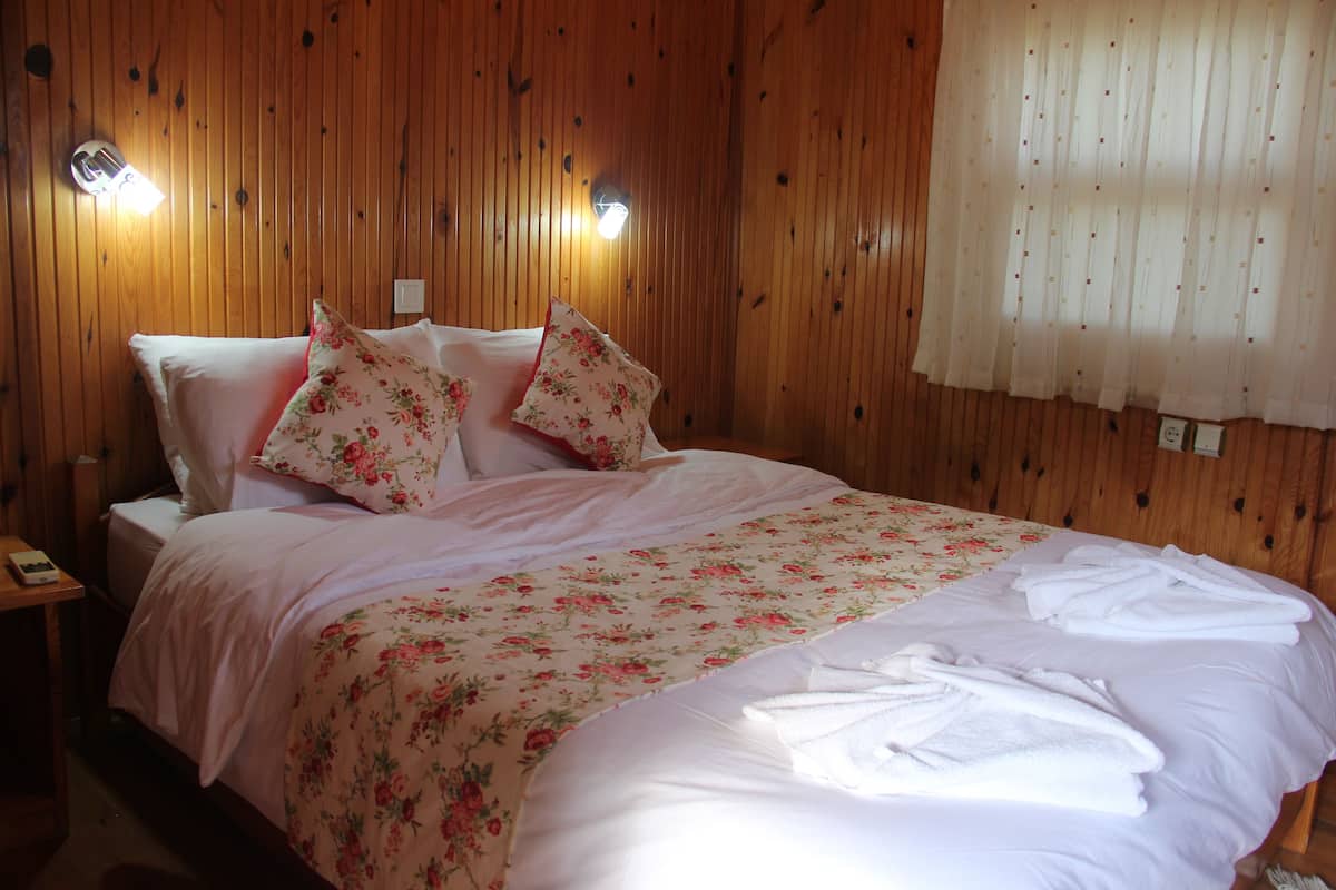 A neatly made bed with floral bedding and white pillows, a bedside table with a lamp, and a window with sheer curtains.