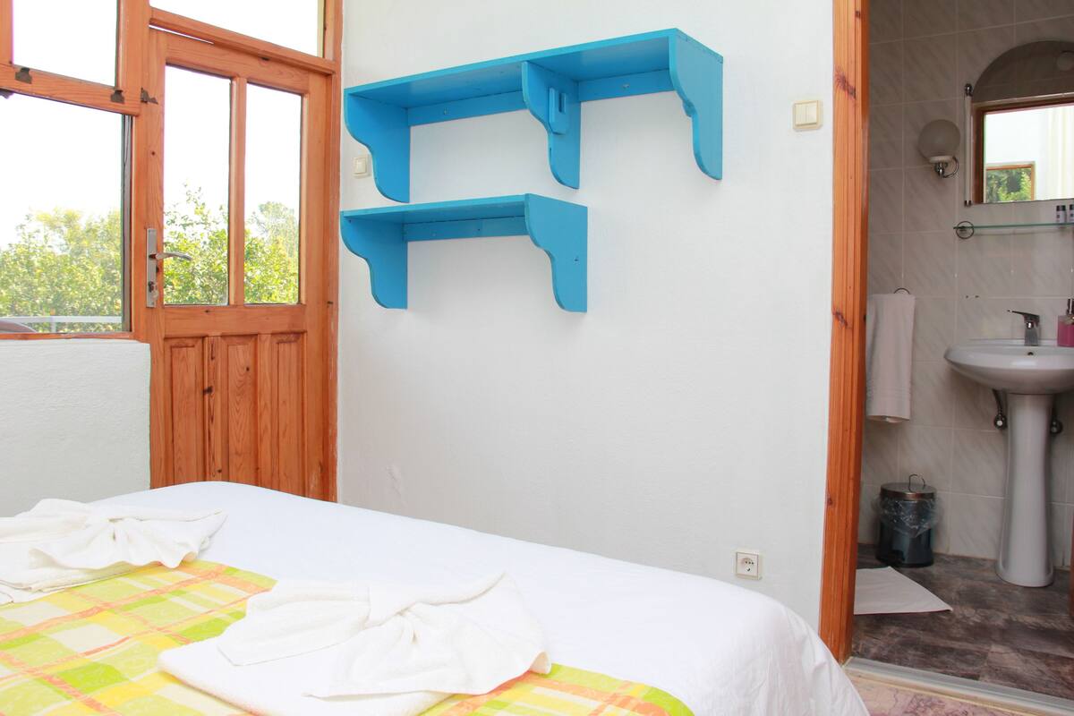 A bedroom with a bed, a window, a bathroom with a sink and mirror, and blue wall shelves.