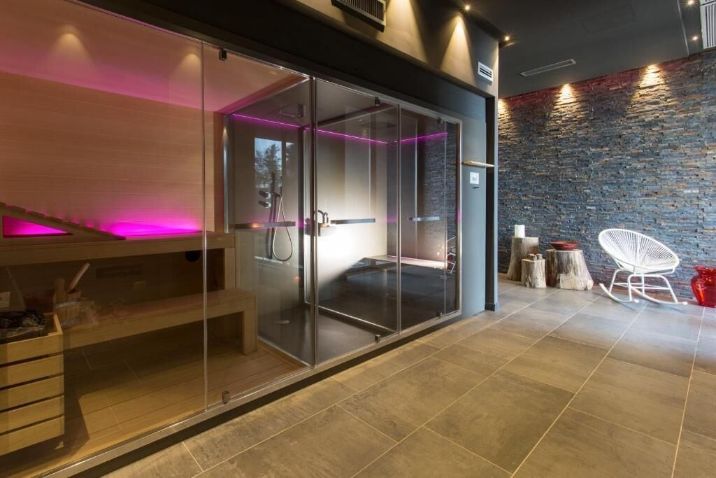 A modern spa room with a glass enclosure, a wooden bench, and a stone wall.