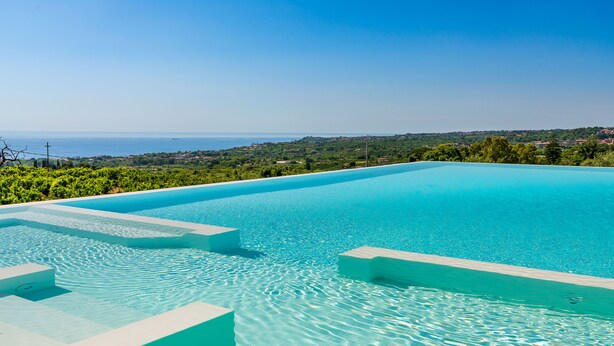 Ein klares, blaues Infinity-Pool mit Blick auf das Meer und eine grüne Landschaft.
