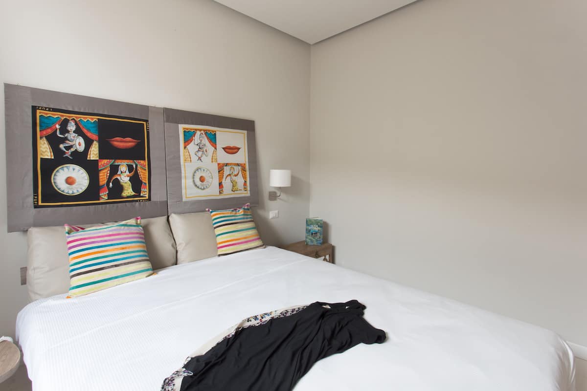 Une chambre d’hôtel avec un grand lit, des coussins rayés aux couleurs vives et un mur orné de tableaux encadrés.