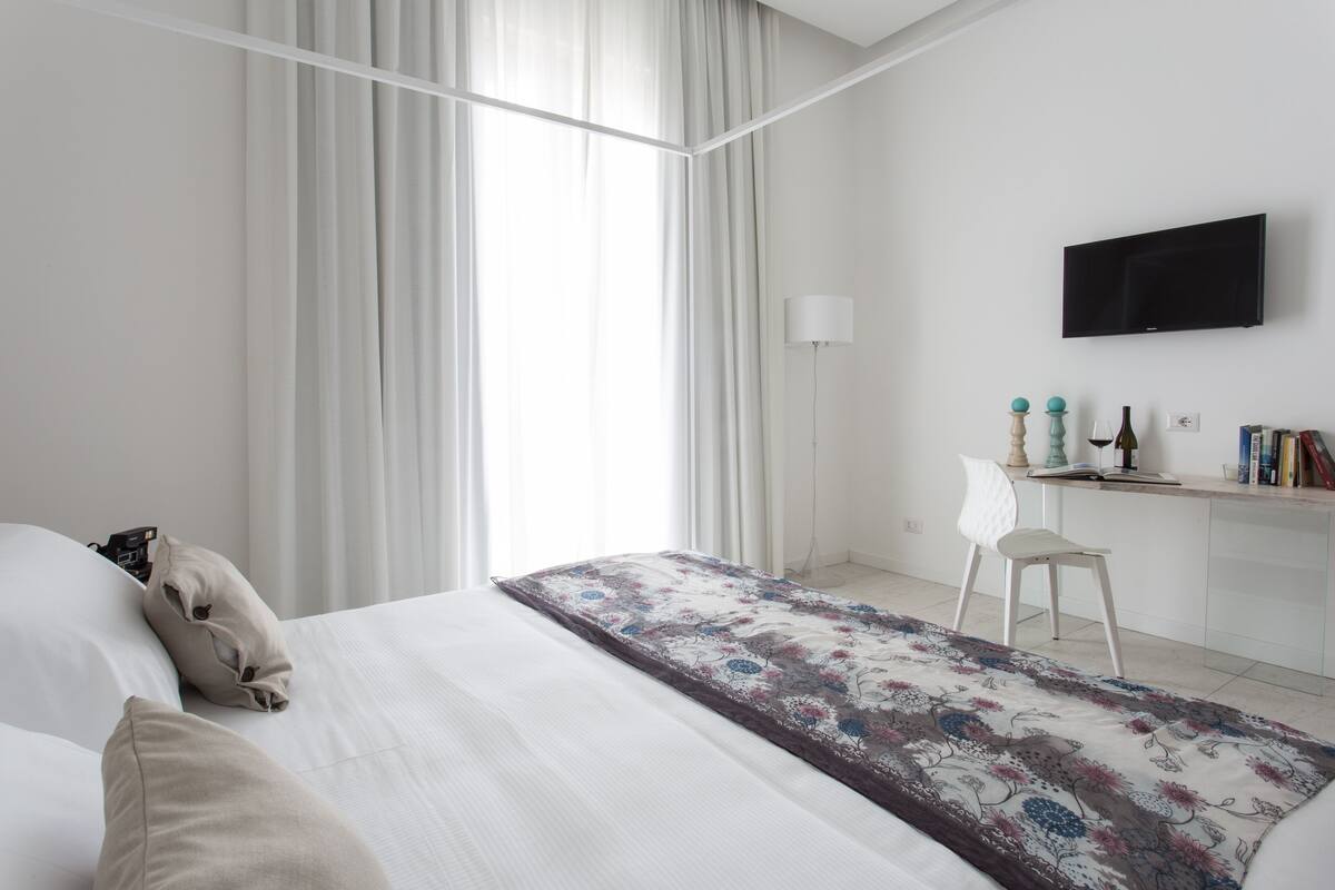 Une chambre d’hôtel moderne, dotée d’un grand lit, d’un bureau, d’une chaise, d’une télévision et d’une fenêtre avec des rideaux.
