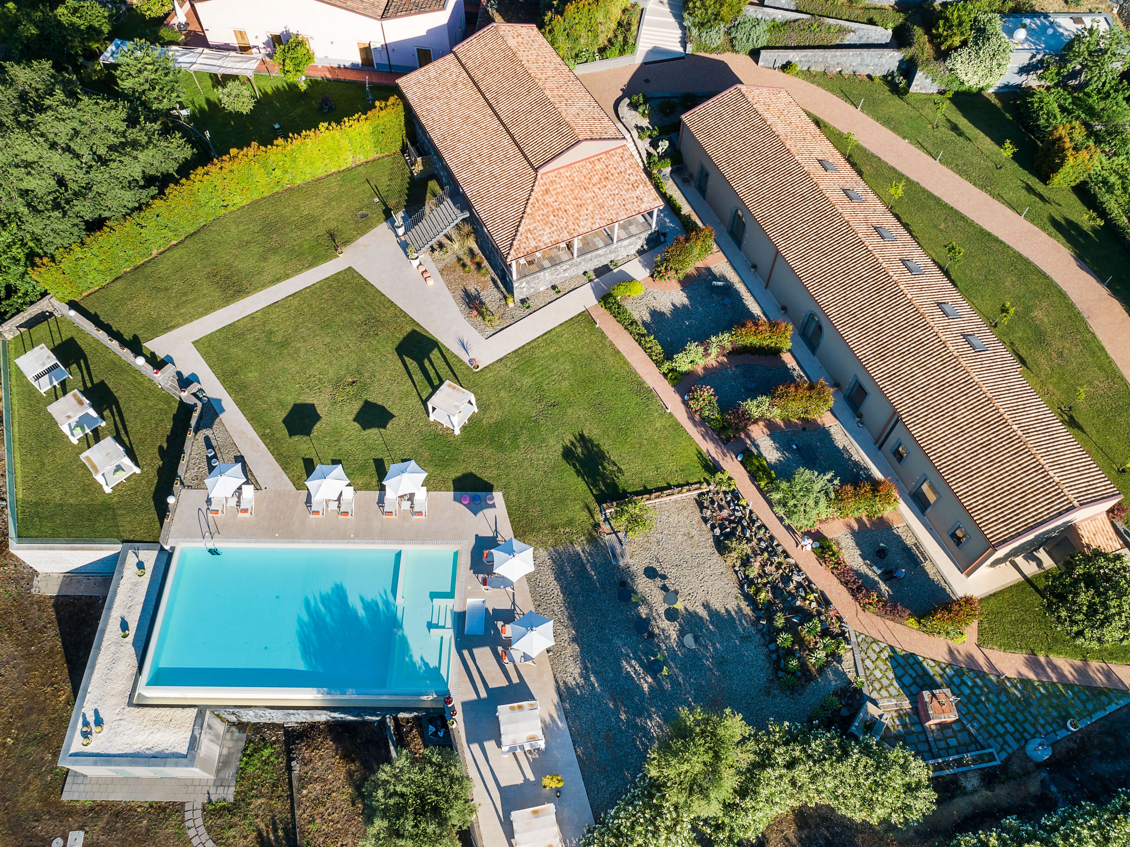 An aerial view of a resort with a swimming pool, sun loungers, and a well-maintained garden.