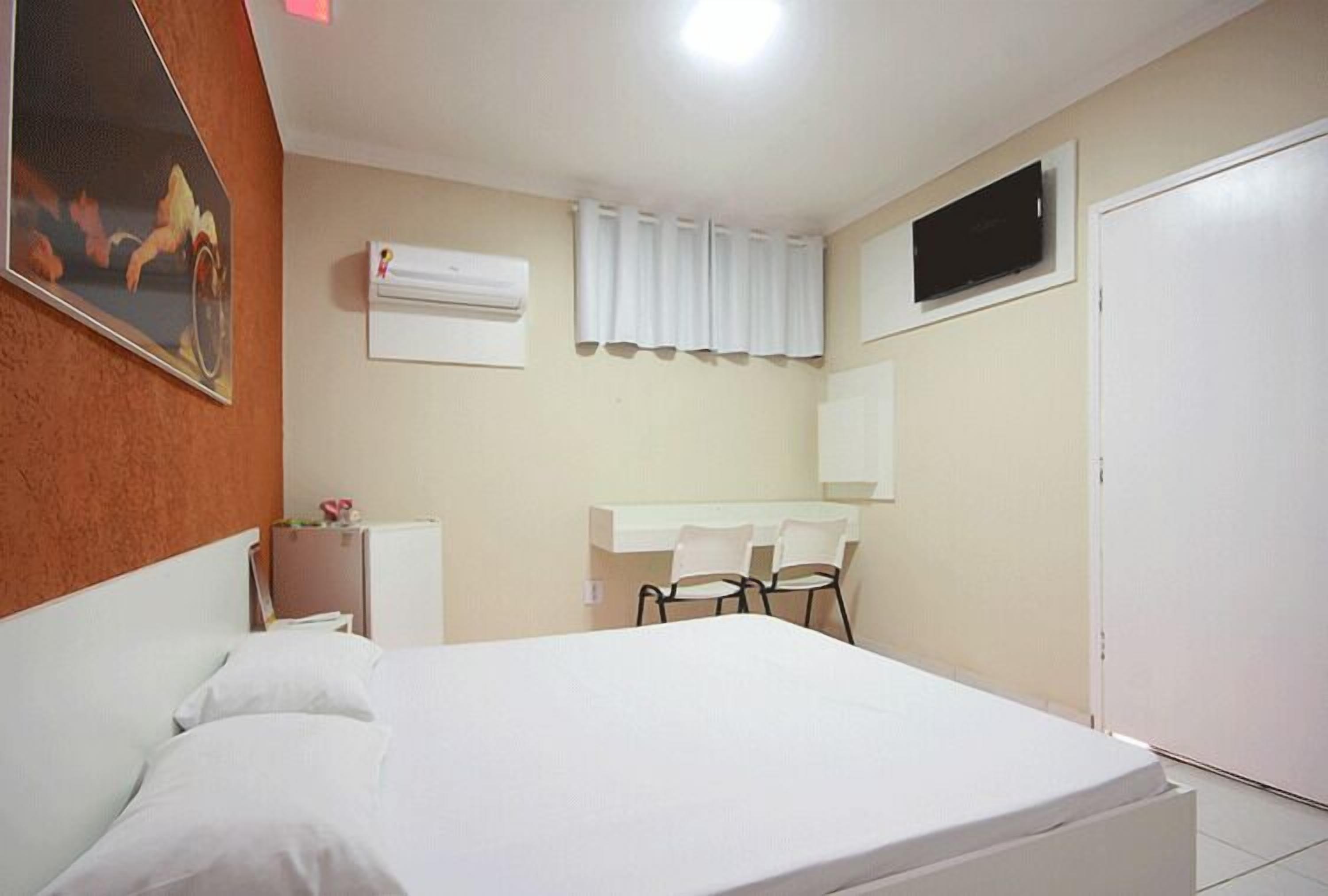 Een hotelkamer met een bed, een bureau met twee stoelen, een televisie en een airconditioner.