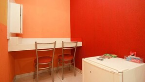 Una habitación pequeña con dos sillas metálicas, un escritorio blanco y un refrigerador blanco.