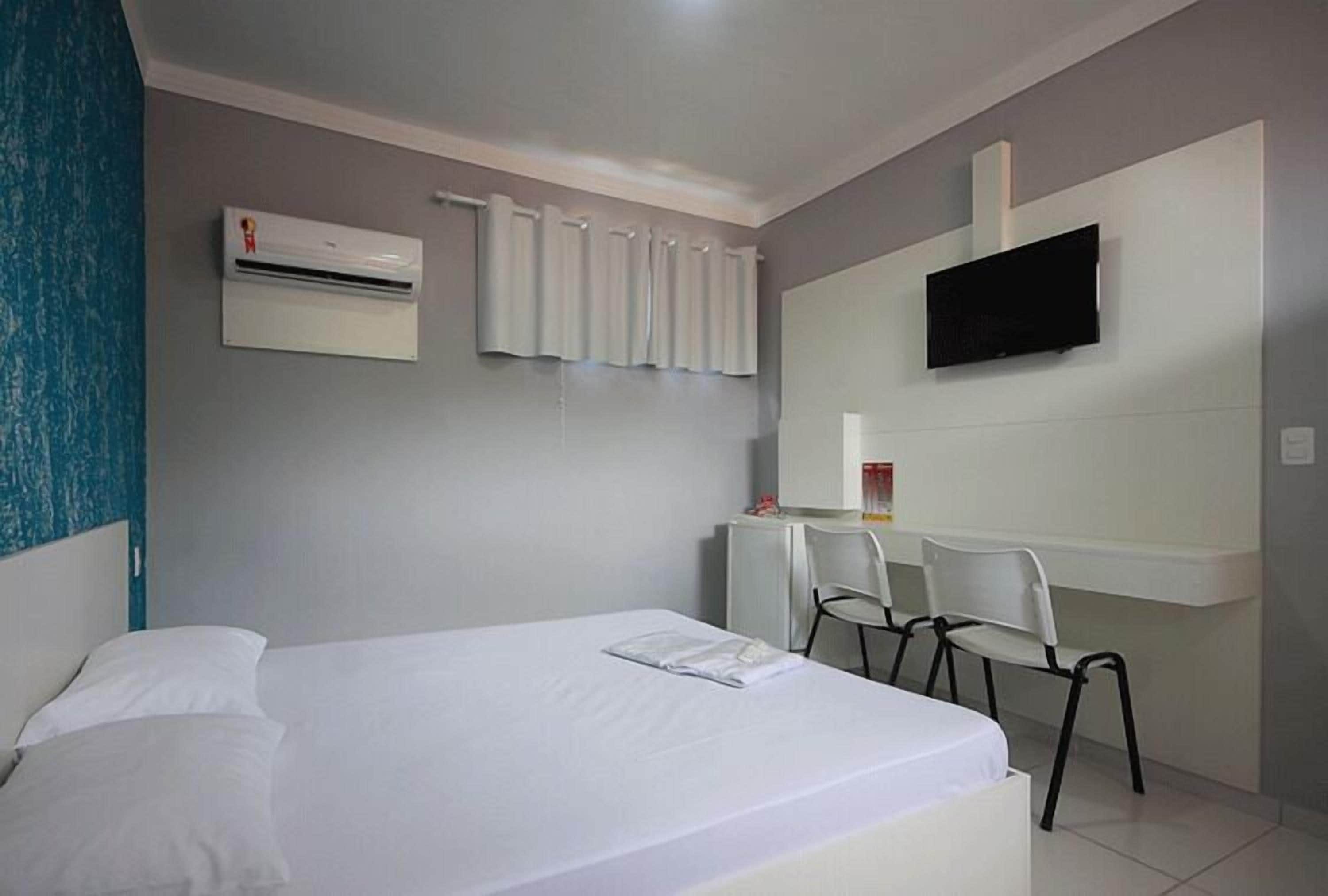 Habitación de hotel con cama, escritorio, dos sillas, televisión y aire acondicionado.