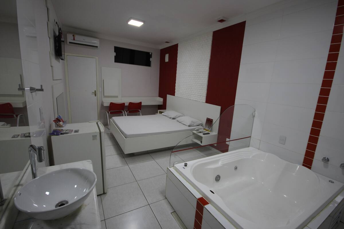Une salle de bain moderne avec une grande baignoire, un lavabo et un lit agrémenté d’oreillers rouges.