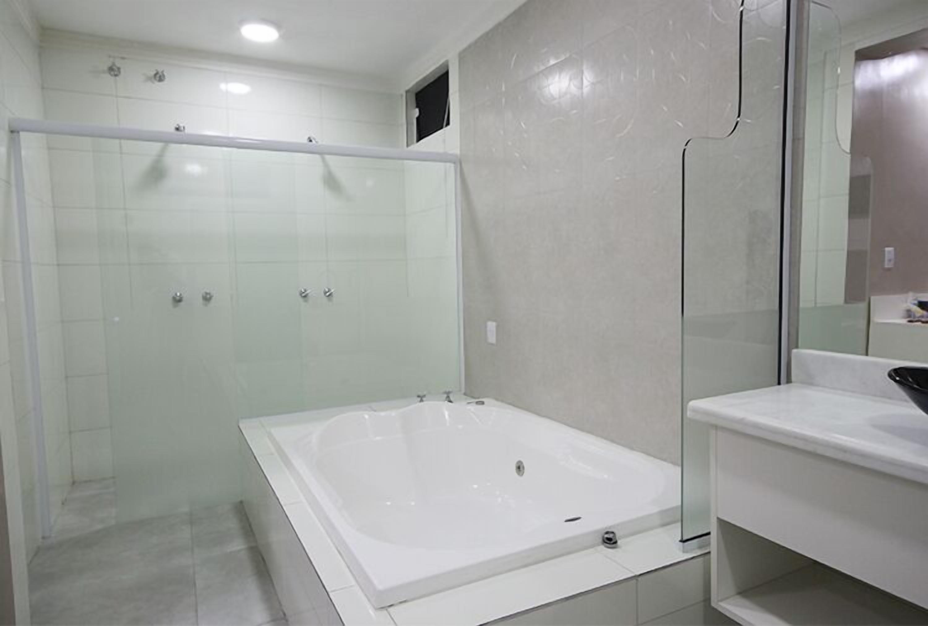 Ein modernes Badezimmer mit einer in Glas abgeschlossenen Dusche, einer großzügigen freistehenden Badewanne und einem weißen Waschtisch mit Spiegel.