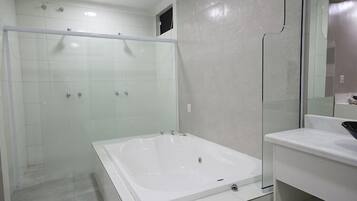 Ein modernes Badezimmer mit einer in Glas abgeschlossenen Dusche, einer großzügigen freistehenden Badewanne und einem weißen Waschtisch mit Spiegel.