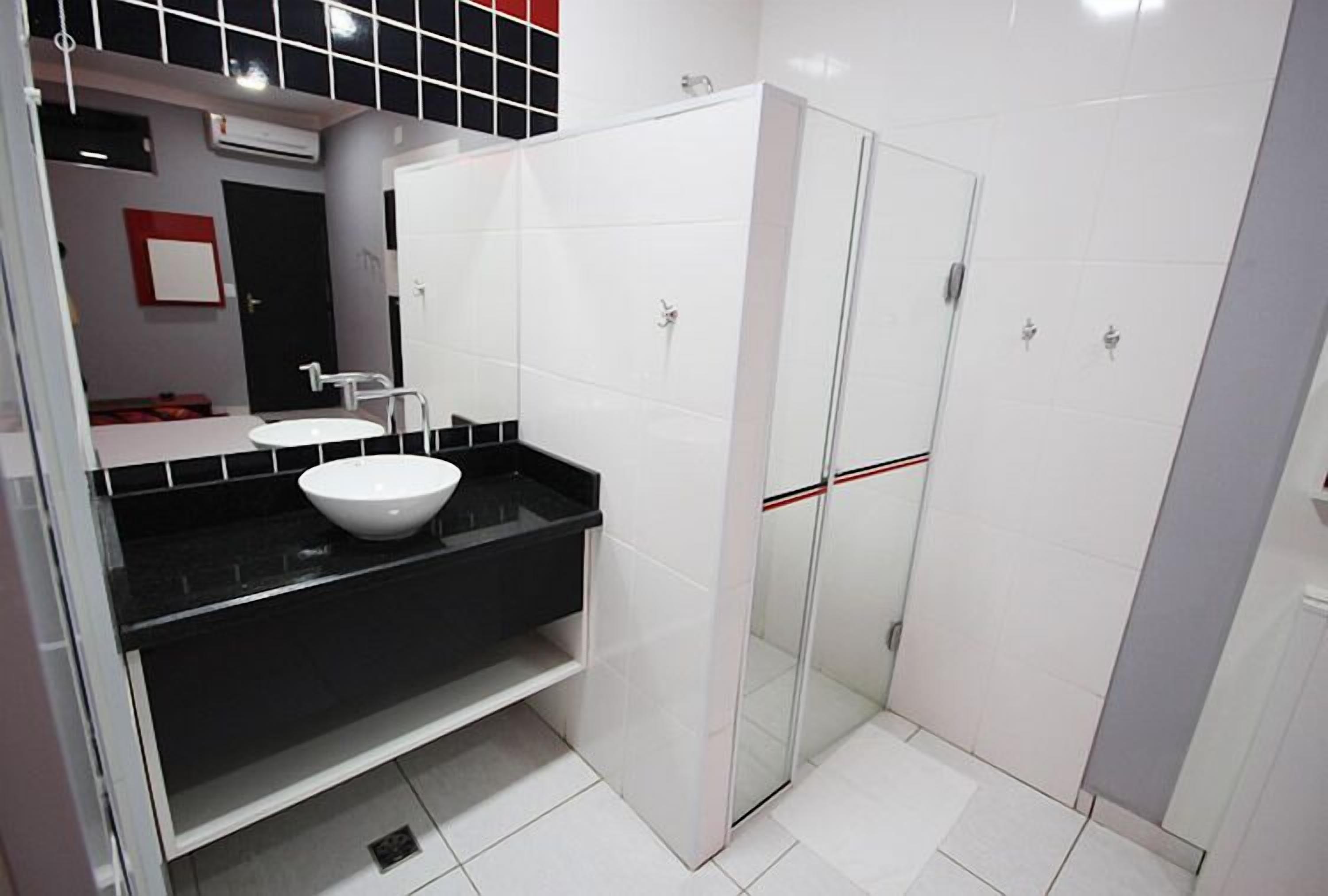 Un baño moderno con lavamanos blanco, encimera negra y zona de ducha con mampara de vidrio.