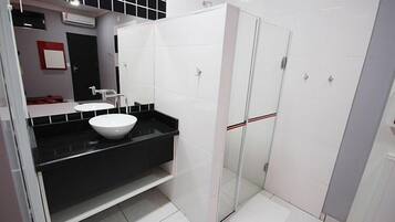 Un baño moderno con lavamanos blanco, encimera negra y zona de ducha con mampara de vidrio.