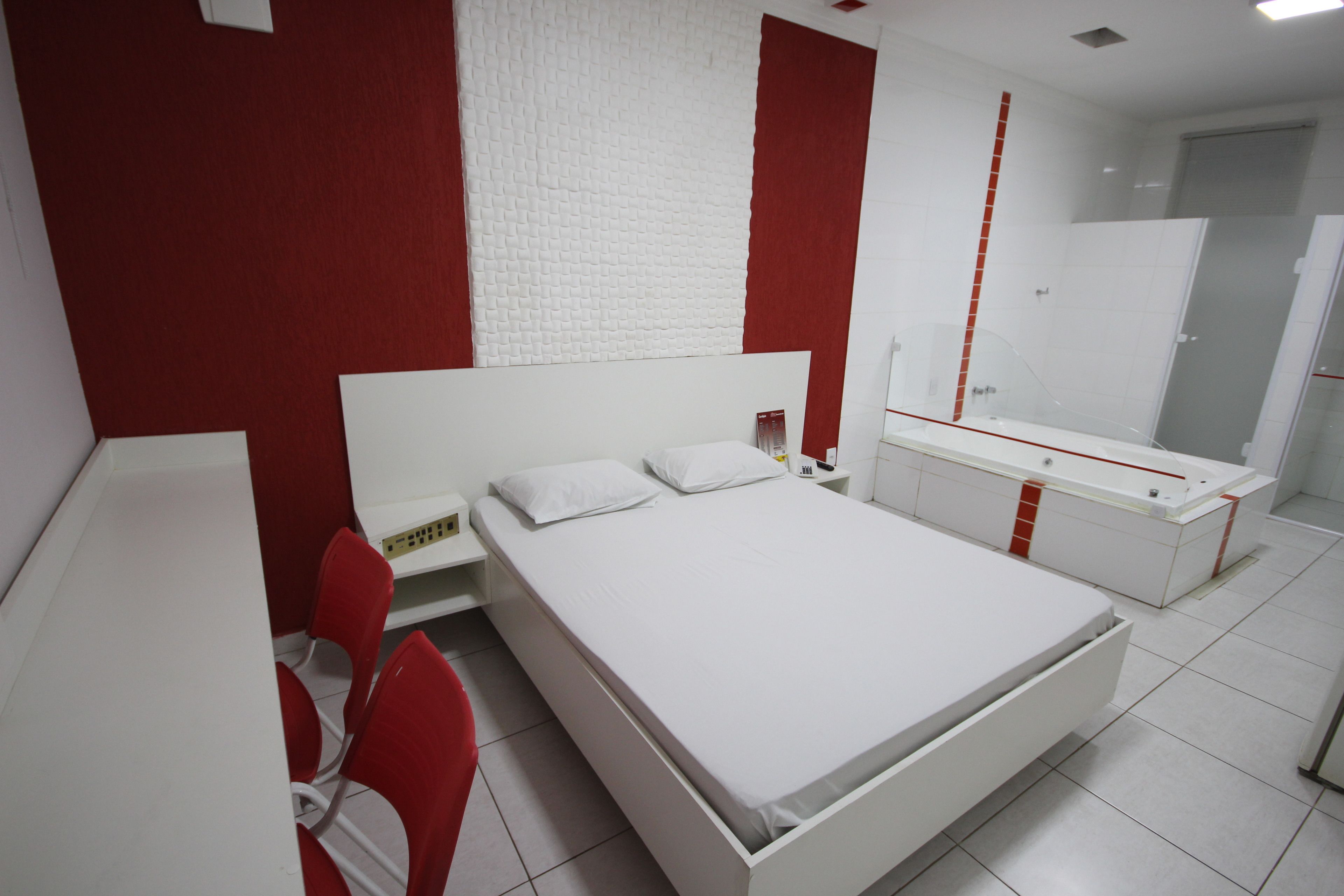 Un dormitorio moderno con una cama blanca, sillas rojas, un armario blanco y una pared texturizada en rojo y blanco.