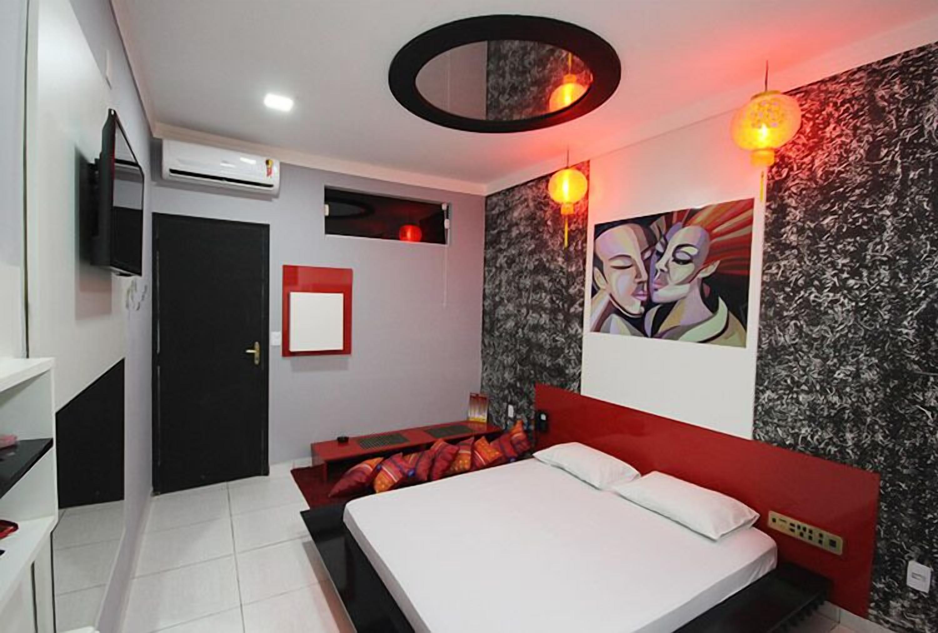 Un dormitorio moderno con una cama, cabecera roja, televisor montado en la pared y un cuadro.