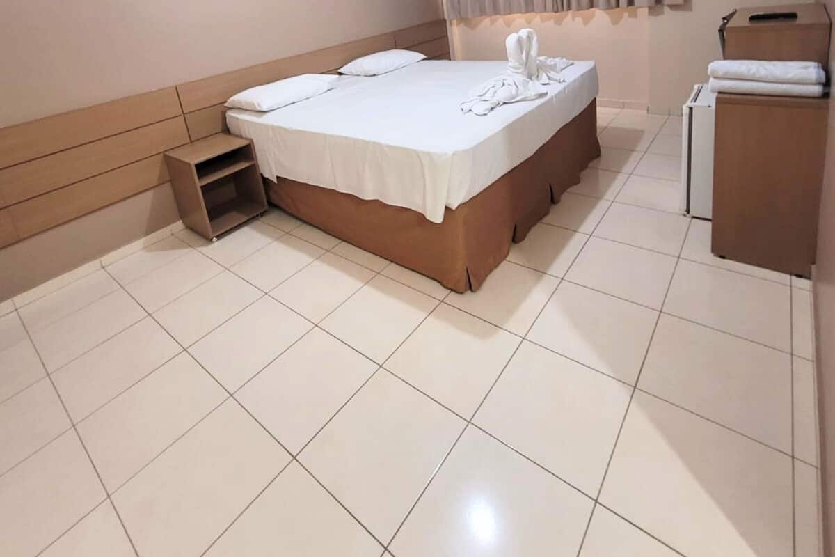 Una habitación de hotel con cama, estante pequeño, escritorio y silla.