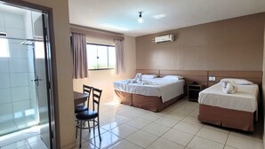 Habitación de hotel con dos camas, una mesa de comedor con sillas, un ventanal corredero y un equipo de aire acondicionado.