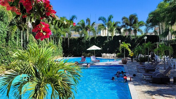 Una piscina con agua azul cristalina, rodeada de palmeras y flores rojas.