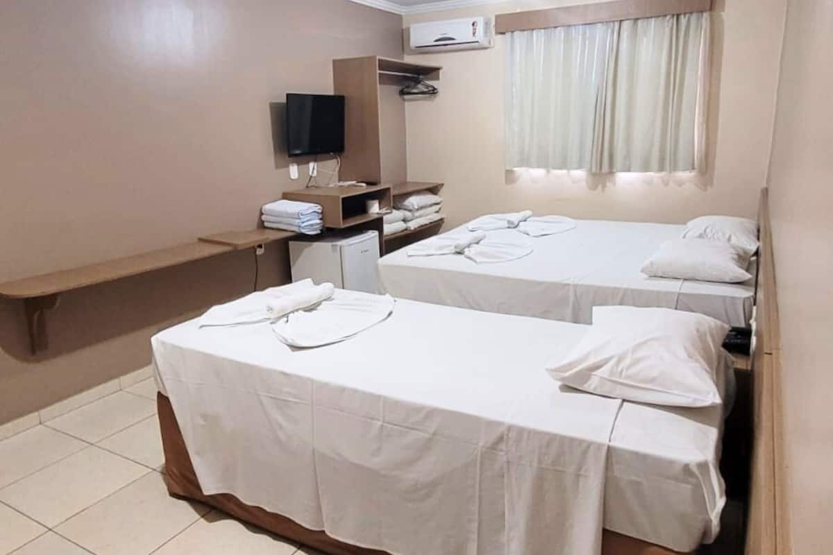Habitación de hotel con dos camas, un televisor, una mesita y una ventana con cortinas.