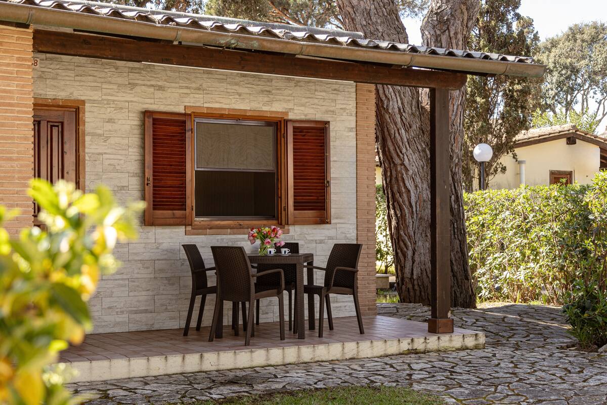 A stone patio with a table and chairs, a pergola, and a brick building with wooden shutters.