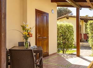 An outdoor patio with wicker furniture, a table with a vase of flowers, and a wooden door. - Holiday Village (Fondi)