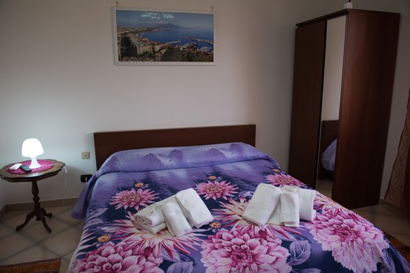 A bedroom with a bed, a bedside table with a lamp, a mirror, and a painting on the wall. - AreA DomuS (Pompei)