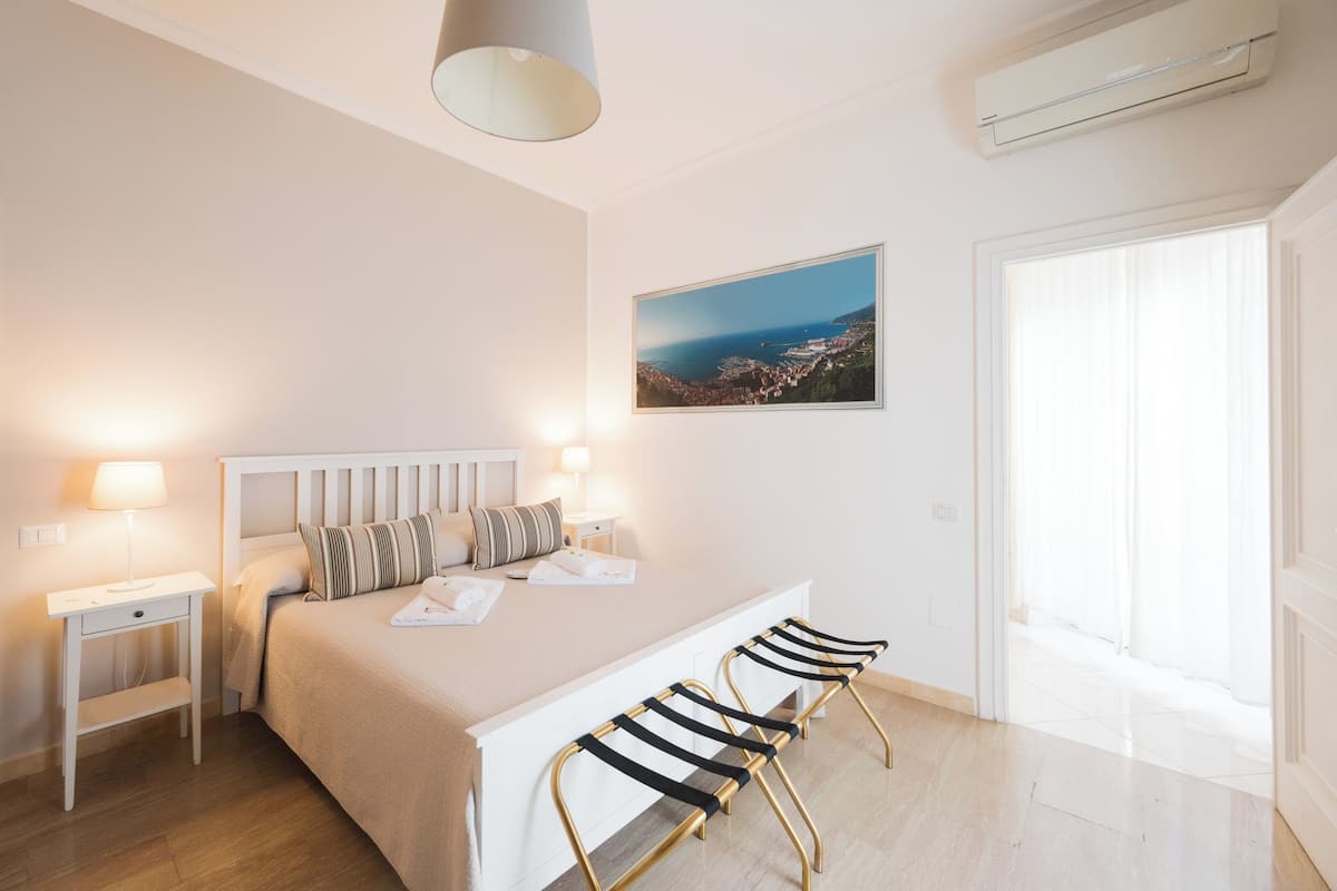 Une chambre à coucher comprenant un lit, des tables de chevet, un bureau, une chaise, une fenêtre et un tableau au mur.