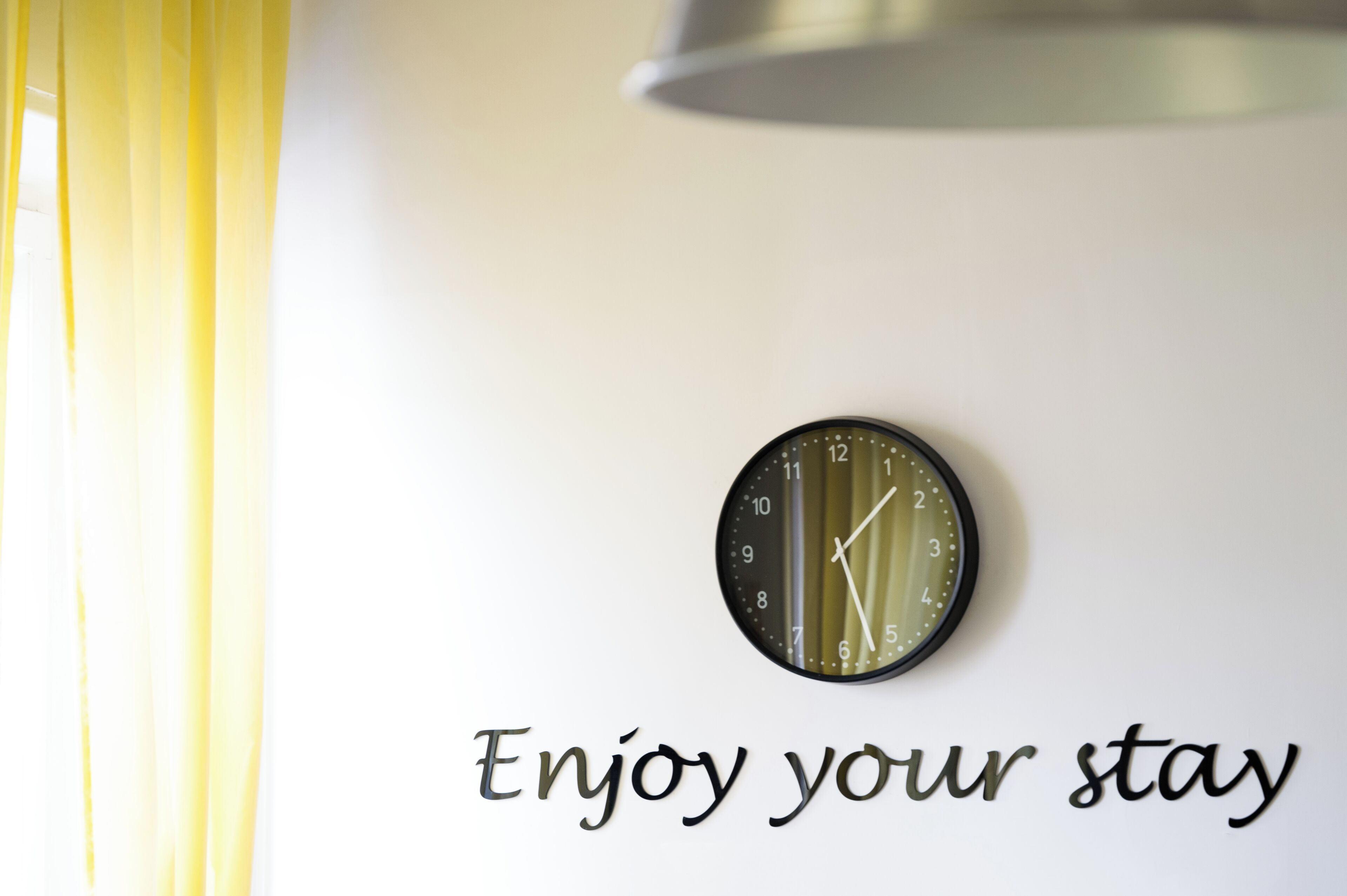 A wall clock and the text "Enjoy your stay" on a white wall.
