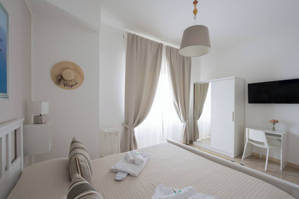 Une chambre d’hôtel équipée d’un lit, d’une table de chevet, d’un miroir, d’un bureau et d’un téléviseur fixé au mur.