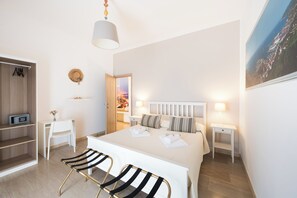 A hotel room with a bed, bedside tables, a desk, a chair, a wardrobe, and a view of a coastal area. - Panoramic Rooms Salerno (Salerno)