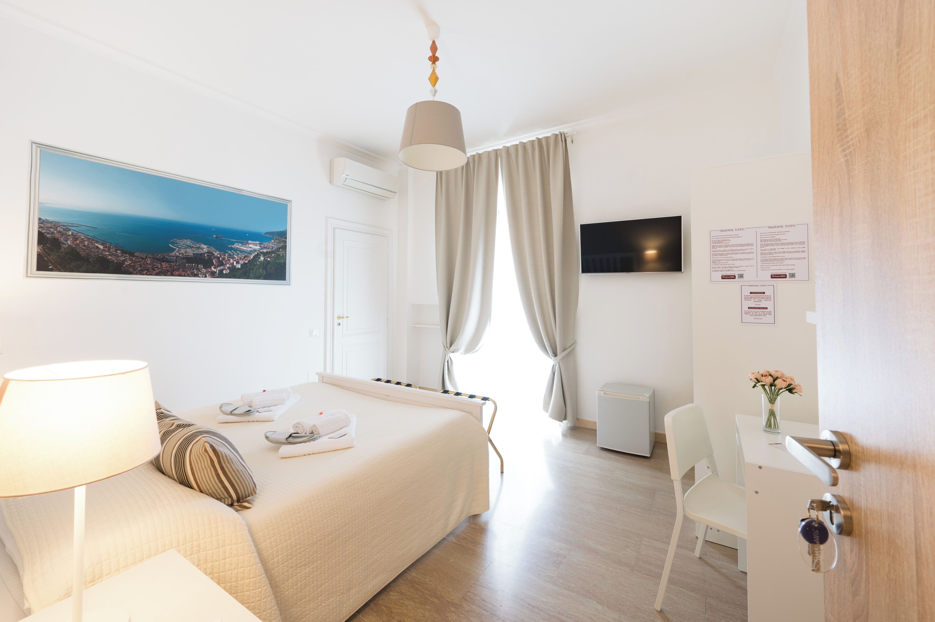 Une chambre d’hôtel équipée d’un lit, d’un bureau, d’une chaise, d’une lampe, d’une télévision et d’une fenêtre avec des rideaux.