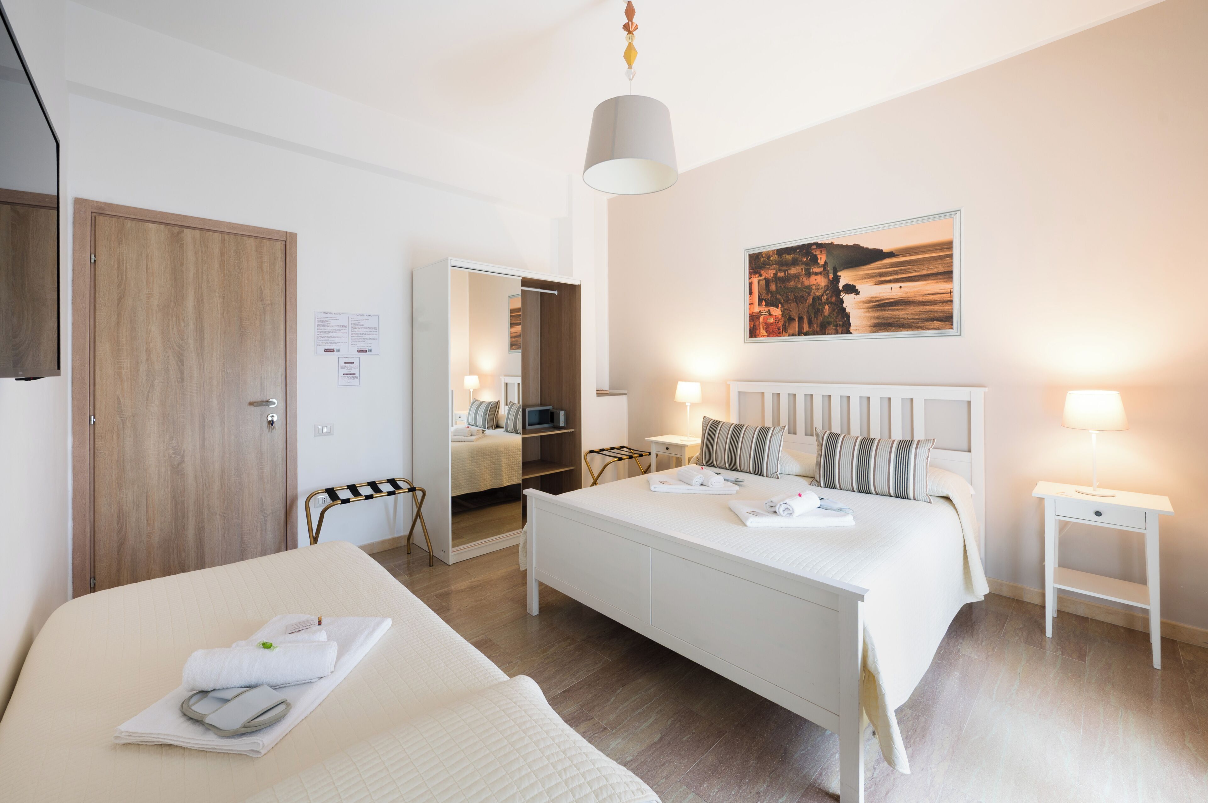 A hotel room with a bed, bedside tables, a wardrobe, a mirror, and a painting on the wall.