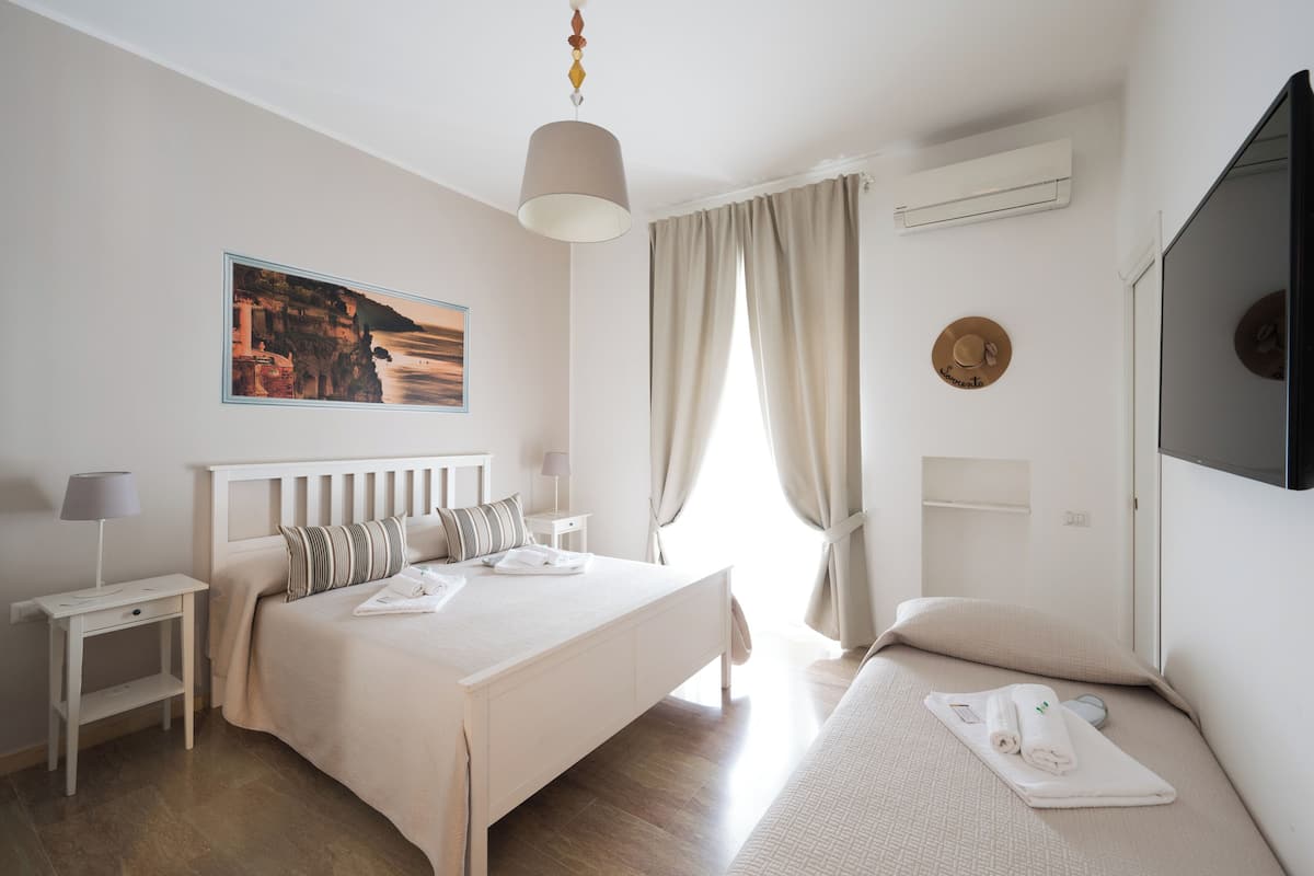 Une chambre d’hôtel avec un lit, une table de chevet, une lampe et un tableau représentant un paysage côtier.