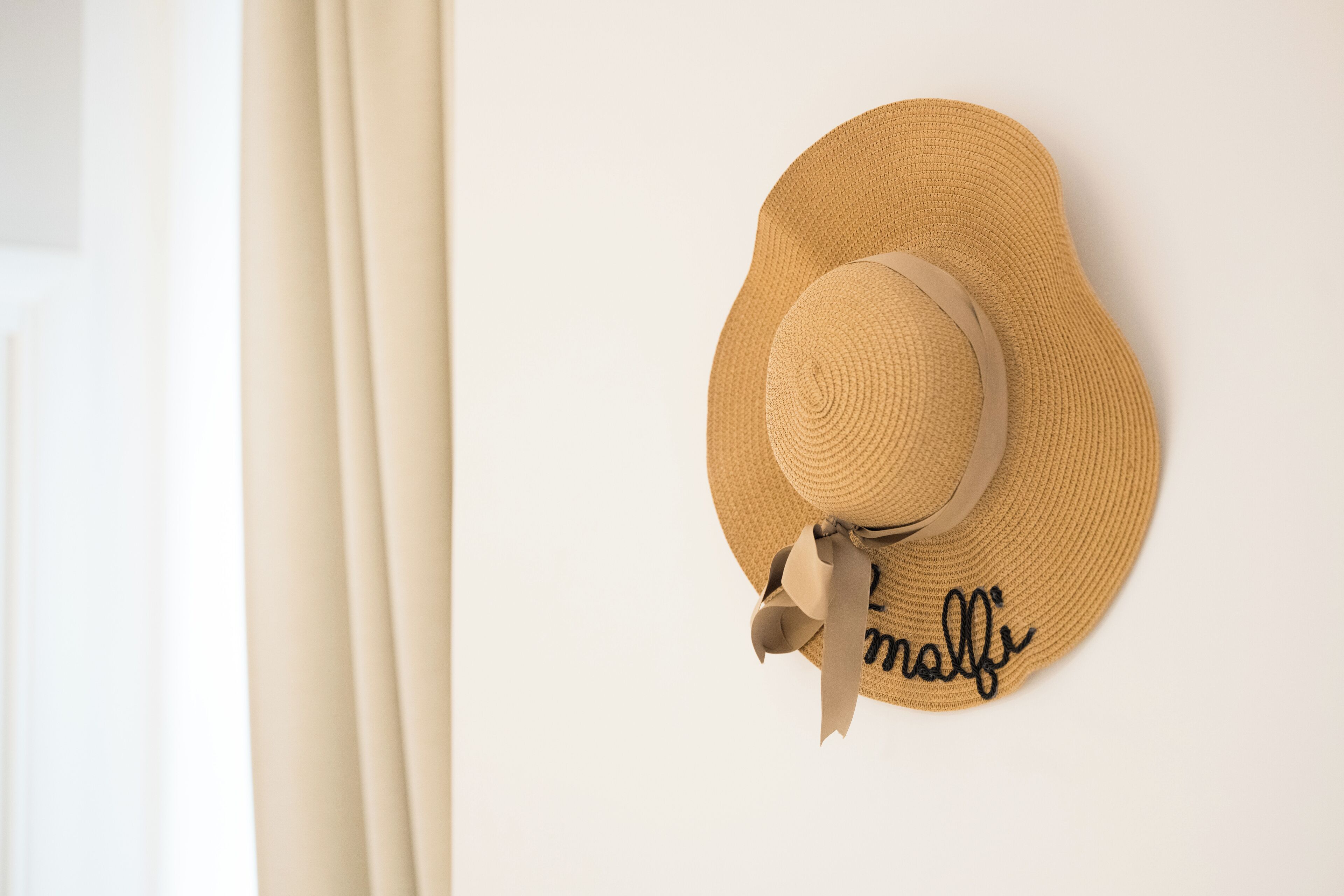 A straw hat with a ribbon and the word "malfi" on a white wall.