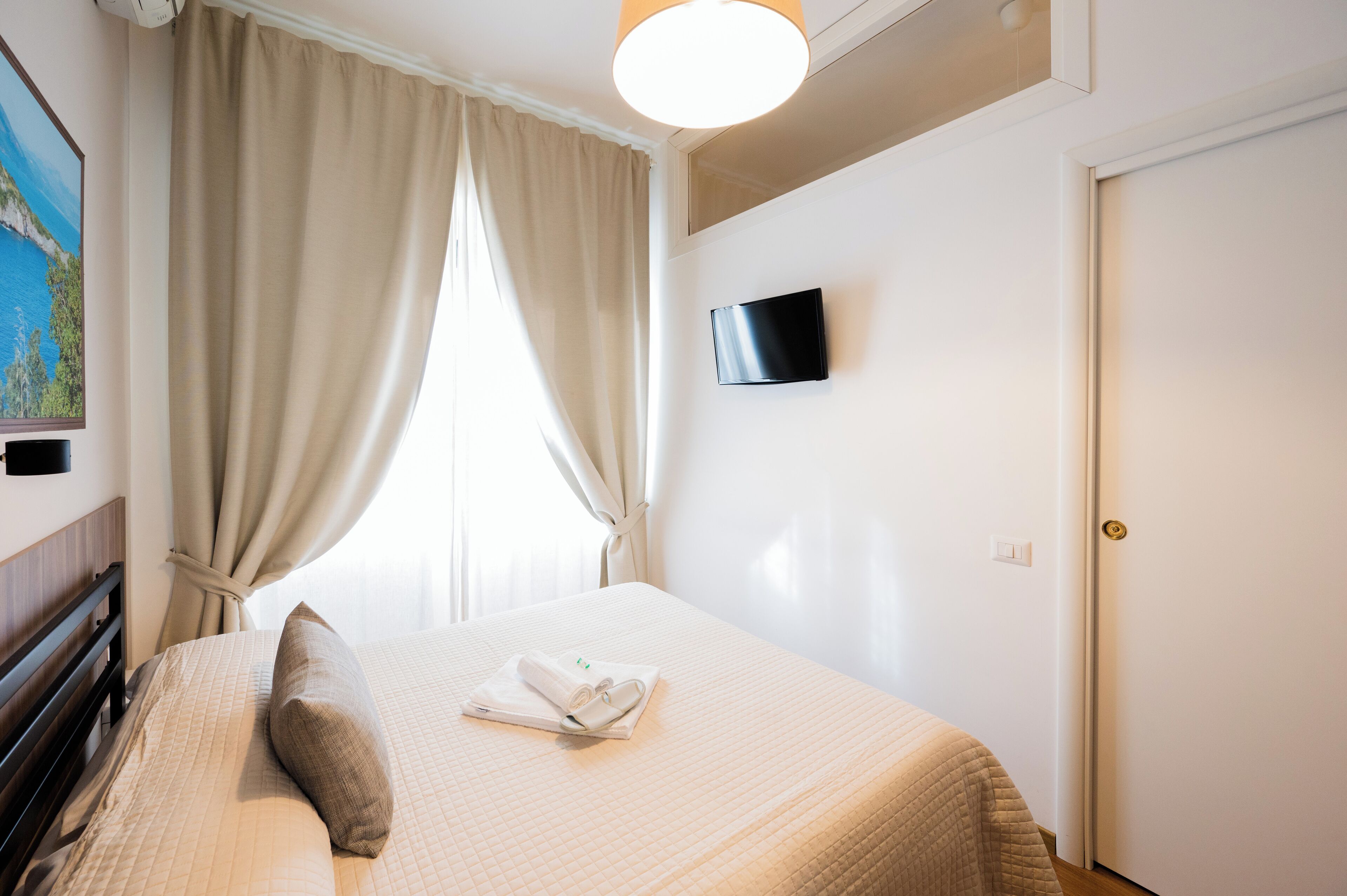 A neatly made bed with a pillow, a folded towel, and a flat-screen TV mounted on the wall.