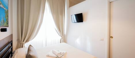Una cama bien hecha con una almohada, una toalla doblada y un televisor de pantalla plana montado en la pared.