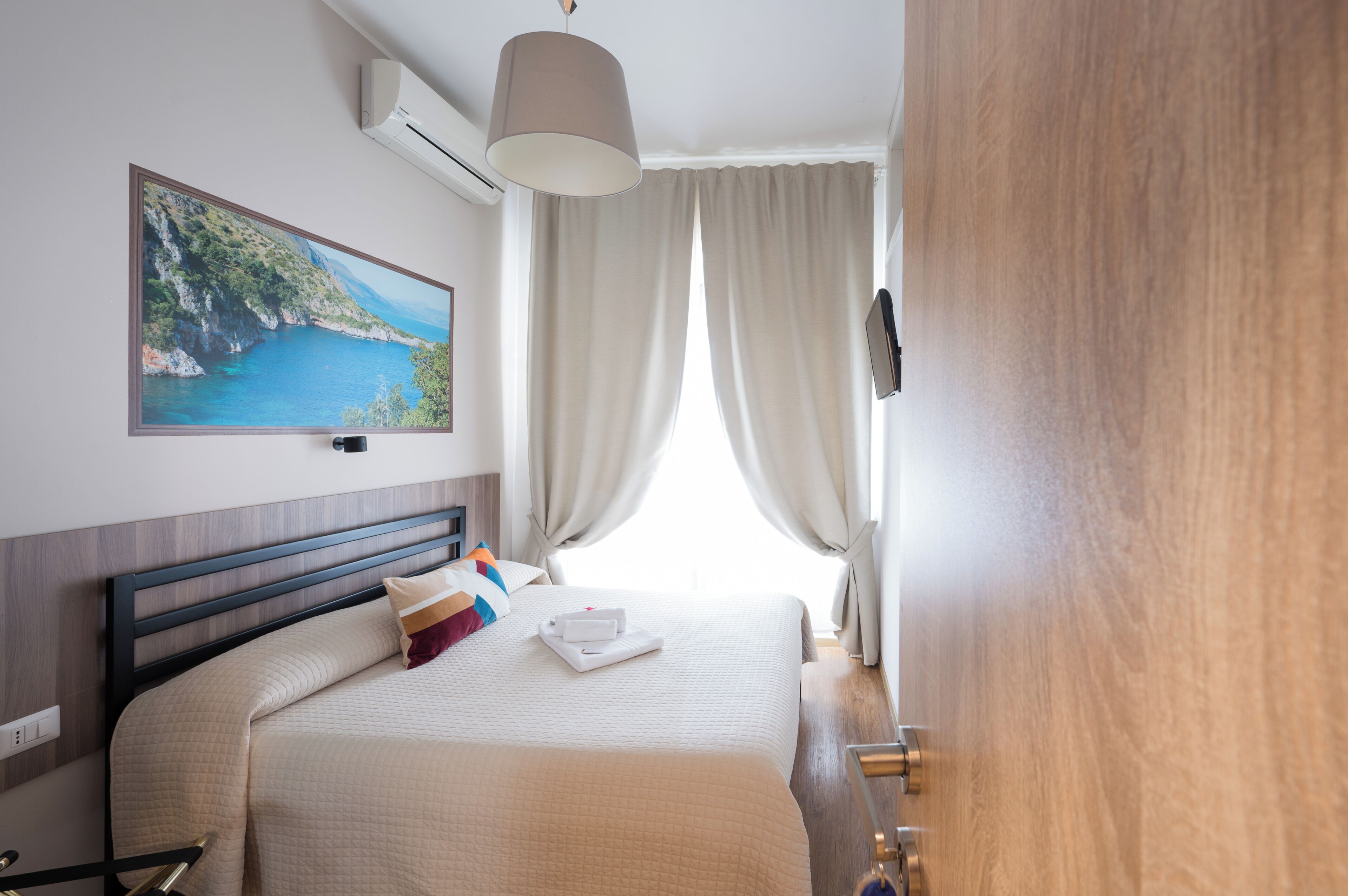 Een hotelkamer met een bed, een schilderij van een kustlandschap, een televisie en een deur.