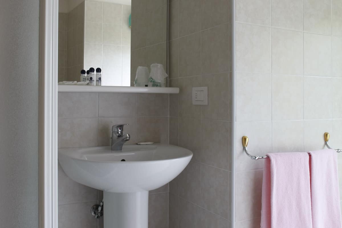 Une salle de bain avec un lavabo sur colonne, un miroir au-dessus, un porte-serviettes avec une serviette rose et une poubelle.
