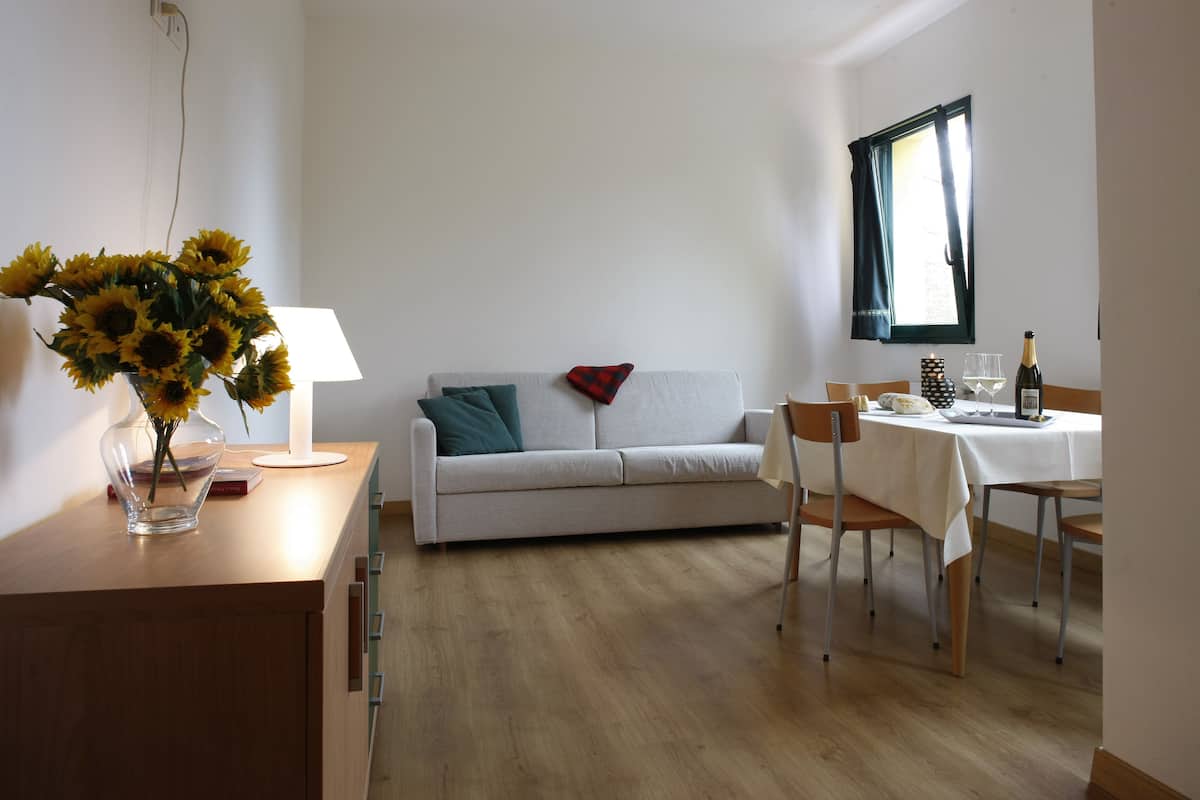 Une pièce comprenant un canapé, une table à manger avec des chaises, un vase avec des fleurs et une fenêtre avec des rideaux.