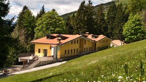 Ein gelbes Gebäude mit rotem Dach, umgeben von einer grünen Wiese und Bäumen.