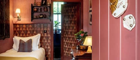 A room with a bed, a desk with a lamp, a door with a sign, and a patterned wall.