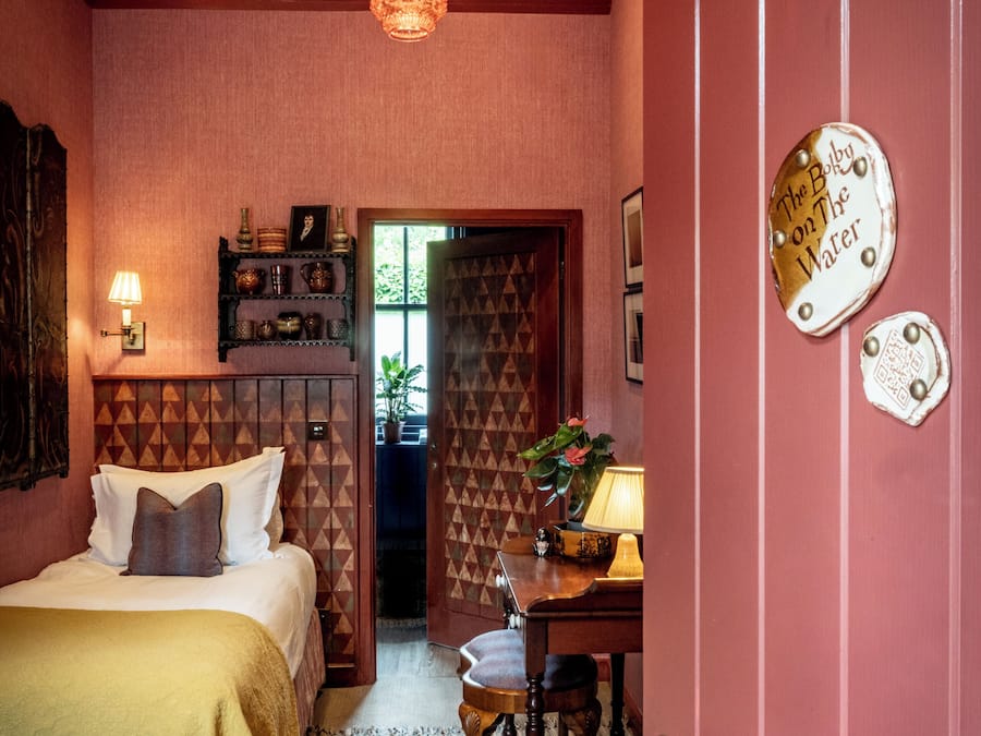 Une pièce avec un lit, un bureau avec une lampe, une porte avec une pancarte et un mur décoré de motifs.
