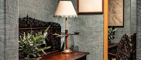 A room with a desk, chair, lamp, and framed artwork on the wall.
