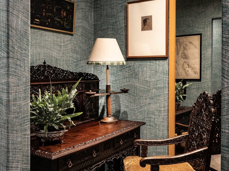A room with a desk, chair, lamp, and framed artwork on the wall.